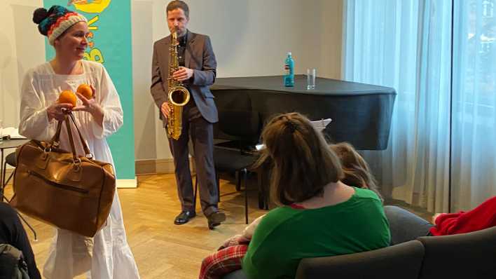Autorin Frauke Angel spielt ihre Geschichte vor den Eltern und Kindern, im Hintergrund spielt Tilman Ehrhorn das Saxophon (Quelle: rbb/OHRENBÄR/Birgit Patzelt)