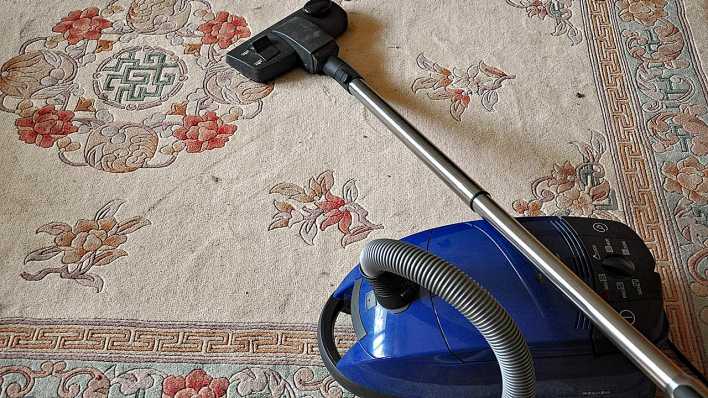 Ein blauer Staubsauger liegt auf einem schmutzigen Teppich (Quelle: imago/Panthermedia)