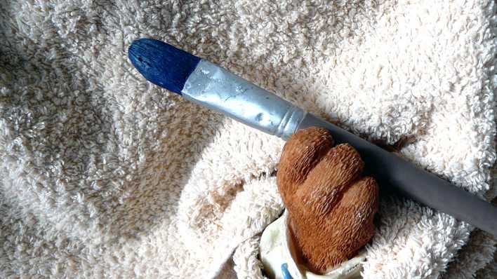 Die Pfote einer Bärenfigur hält einen Pinsel mit blauer Farbe (Quelle: rbb/OHRENBÄR/Sonja Kessen)