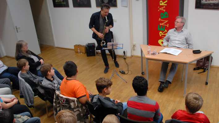 Kinder schauen zu Musiker Falk Breitkreuz, er spielt Klarinette, Autor Herbert Beckmann am Tisch daneben (Quelle: rbb/OHRENBÄR/Birgit Patzelt)