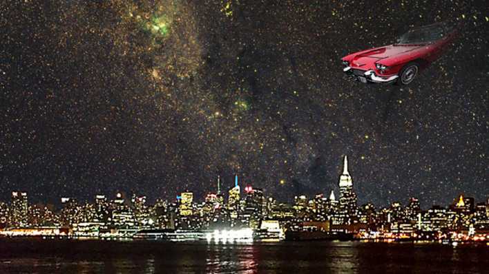 Ein rotes Auto fliegt bei Nacht über einer beleuchteten Stadt am Meer (Quelle: H. D. Tylle)