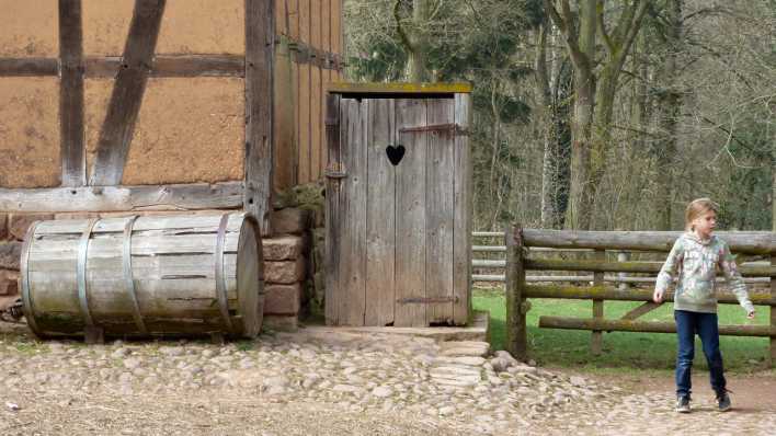 Ein altes Fachwerkhaus, daneben ein Holzhäuschen mit Herz in der Tür und ein junges Mädchen schaut zur Seite (Quelle: rbb/OHRENBÄR/Sonja Kessen)