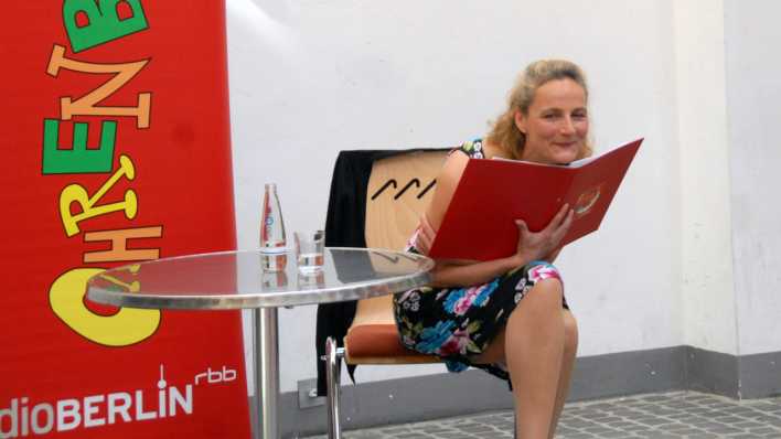 Schauspielerin Marion Elskis liest eine OHRENBÄR-Radiogeschichte, im Hintergrund das OHRENBÄR-Banner (Quelle: rbb/OHRENBÄR/Birgit Patzelt)