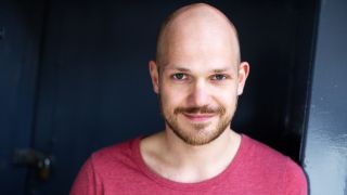 Porträt des Schauspielers Matti Krause, mit himbeerfarbenem T-Shirt, vor einer blauen Tür (Quelle: Hannes Caspar)