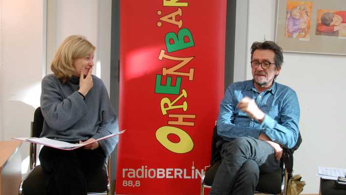 Autorin Anja Frisch und Musiker Ralf Schmidt, sitzend, hinter ihnen ein OHRENBÄR-Banner (Quelle: rbb/OHRENBÄR/Birgit Patzelt)