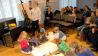 Sandra Bach mal live zur Geschichte, im Hintergrund OHRENBÄR-Autor Hubert Schirneck liest, davor: Kinder malen auf Blätter, die auf dem Boden liegen (Quelle: rbb/OHRENBÄR/Birgit Patzelt)