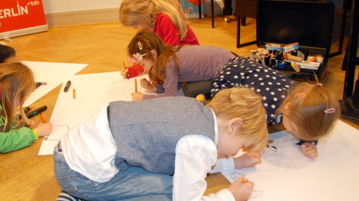 Kinder hocken auf dem Boden und malen auf großen, weißen Blättern (Quelle: rbb/OHRENBÄR/Birgit Patzelt)