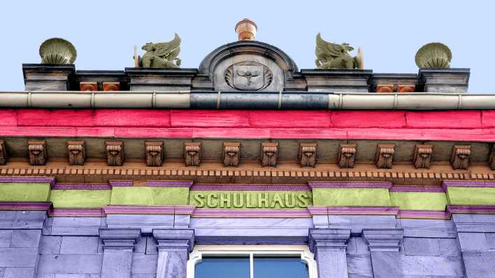 Ein Backsteinhaus aus der Froschperspektive, mit farbigen Backsteinen und dem Schriftzug "Schule" (Quelle: Colourbox)
