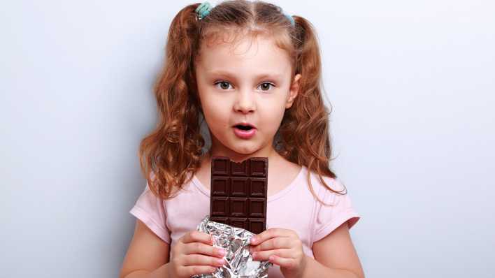 Mädchen mit Zöpfen, etwas Schokolade am Mund, in den Händen eine angebissene Tafel Schokolade (Quelle: Colourbox)