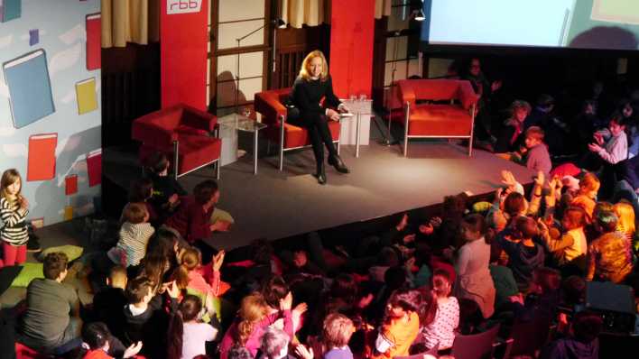 rbb-Intendantin Patricia Schlesinger liest auf der Bühne, im Publikum viele Kinder und wenige Erwachsene (Quelle: rbb/OHRENBÄR/Sonja Kessen)