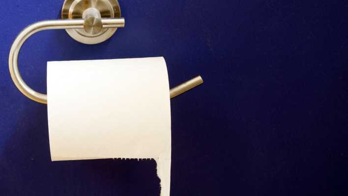 Toilettenpapier-Halter mit einer Rolle Toilettenpapier, an einer lilafarbenem Wand (Quelle: imago images/Mint Images)