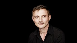 Porträt des Schauspielers Florian Lukas, mit schwarzem Hemd vor dunklem Hintergrund (Quelle: Jan Rickers)