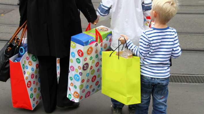 Ein kleiner Junge tröägt eine große, gelbe Einkaufstasche, weitere mit großen Einkaufstaschen davor (Quelle: Imago/ Geisser)