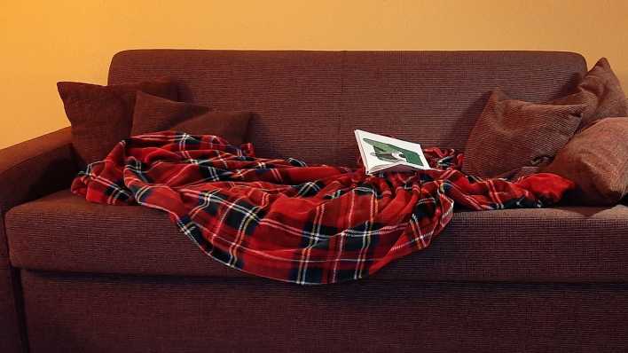 Eine gemütliche Couch, darauf Decke, Buch und Kissen (Quelle: (rbb/OHRENBÄR/Sonja Kessen)