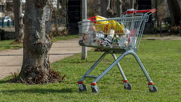 Ein Einkaufswagen, abgestellt auf einer Rasenfläche, voll mit Plastikbechern, Dosen, Einkaufstüten ... (Quelle: imago/Klaus W. Schmidt)