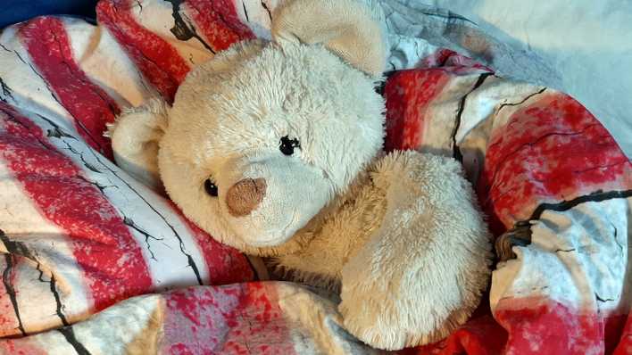 Ein Teddybär, eingekuschelt in eine bunte Decke (Quelle: rbb/OHRENBÄR/Sonja Kessen)