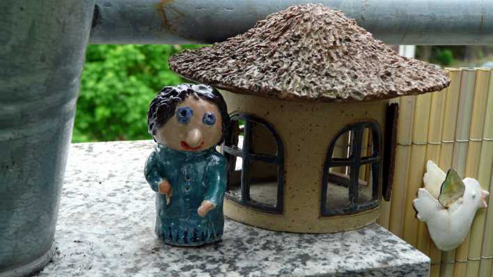 Auf einer Tischplatte aus hellem Marmor: ein gebasteltes Haus und eine kleine Frau als Tonfigur (Quelle: Karin Gähler)