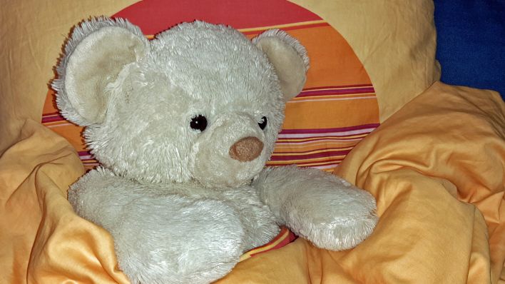 Ein Teddybär, der eingekuschelt in einer hellen Decke ist (Quelle: rbb/OHRENBÄR/Sonja Kessen)