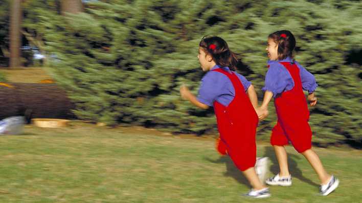 Zwei Mädchen, Zwillinge und gleich gekleidet, laufen im Wald, eine forsch vorn, die andere etwas bedächtiger dahinter (imago/Panthermedia)