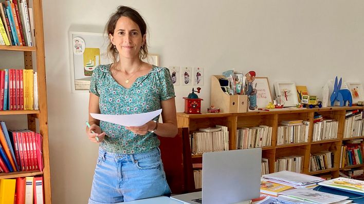 Illustratorin Ariane Camus, steht am Schreibtisch, in den Händen hält sie Zettel und Stift (Quelle: Marko Pauli)