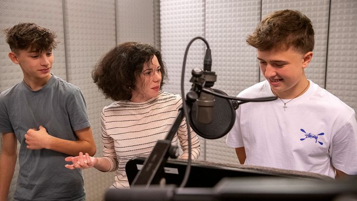 Matti Kaminski (Leon) und Valentin Karow (Ilyas) bekommen Tipps von Regisseurin Marie Lilli Beckmann, im Studio vor einem Mikrofon (Quelle: rbb/OHRENBÄR/Oliver Ziebe)