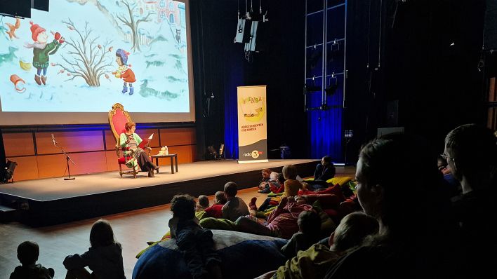 Blick vom Publikum auf die Bühne, Susanne Friedmann liest, im Hintergrund ein weihnachtliches Bild (Quelle: rbb/OHRENBÄR/Sonja Kessen)