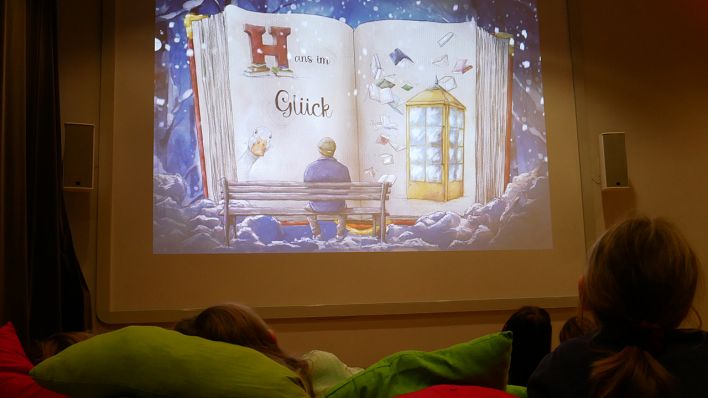 Kinder kuscheln sich in Kissen, im Hintergrund auf der Leinwand Zeichnung eines Buches "Hans im Glück" (Quelle: rbb/OHRENBÄR/Birgit Patzelt)