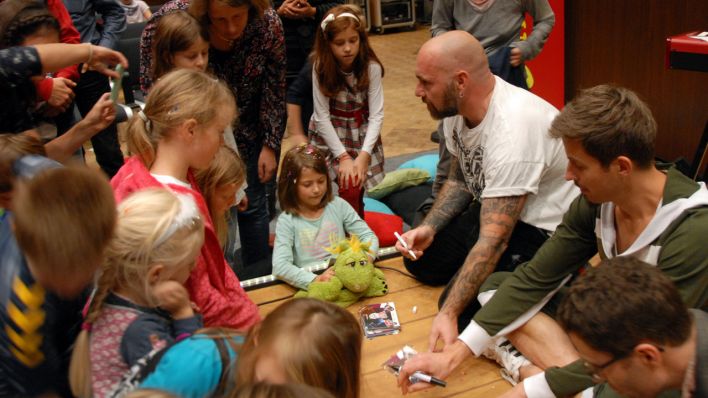 Sänger Kai Lüftner mit den Kollegen vom Rotz'n'Roll Radio geben Autogramme, drumherum Kinder (Quelle: rbb/Birgit Patzelt)