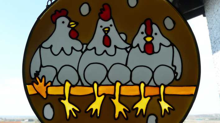 Braunes Schild mit gemaltem Hahn und zwei Hühnern daneben, alle sitzen auf einer Stange (Quelle: rbb/OHRENBÄR/Sonja Kessen)