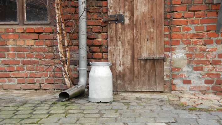 Blick auf eine Schuppenwand mit Holztür und Regenrinne, eine Milchkanne davor (Quelle: rbb/OHRENBÄR/Birgit Patzelt)