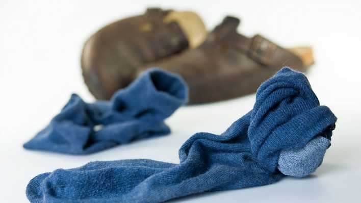 Zwei getragene blaue Socken und im Hintergrund braune Pantoffeln auf dem Boden (Quelle: imago/Mc PHOTO)