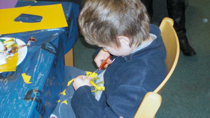 Ein Junge im blauen Pullover schneidet mit einer Schere Papier. © rbb/OHRENBÄR