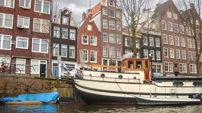 Grachte in Amsterdam mit Häusern und einem Hausboot im Vordergrund (Quelle: Colourbox)