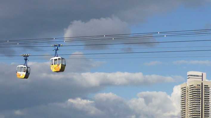 Eine Seilbahn mit zwei gelben Gondeln, am rechten Rand ein Hochhaus, aus der Froschperspektive (Quelle: rbb/OHRENBÄR/Alja Mai)