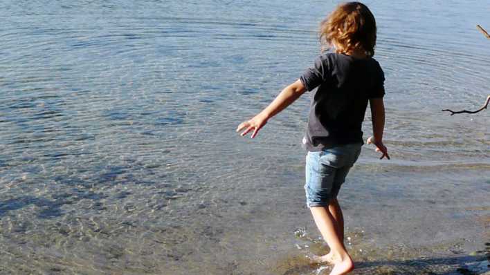 Ein Kind mit kurzen Hosen und Pulli geht vorsichtig ins Wasser (Quelle: rbb/OHRENBÄR/Sonja Kessen)