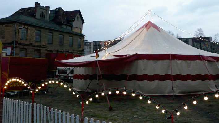 Ein rot-weißes Zirkuszelt neben einem Wohnhaus am Abend (Quelle: rbb/OHRENBÄR/Sonja Kessen)