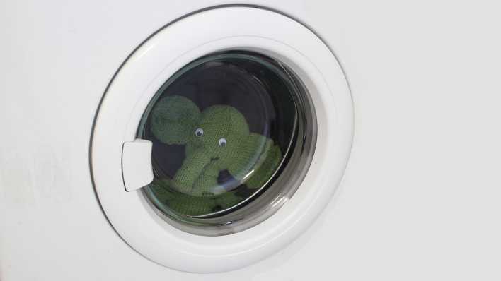 Ein grüner Elefant aus Stoff schaut aus einer echten Waschmaschine (Quelle: Antje Rittermann)