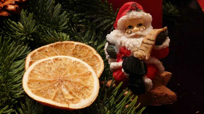 Eine Weihnachtsmannfigur und getrocknete Orangenscheiben auf einem Tannenzweig (Quelle: rbb/OHRENBÄR/Sonja Kessen)