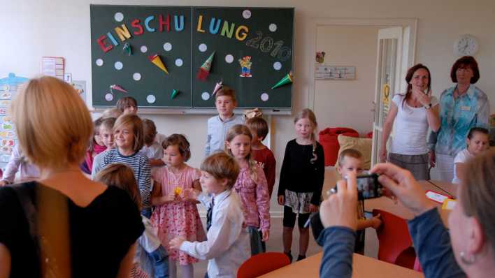 Eine Frau fotografiert den Klassenraum mit Kindern bei der Einschulung (Quelle: imago/Thomas Müller)