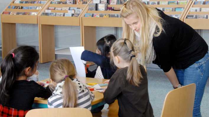 Workshopleiterin erklärt Kindern, die am Tisch sitzen und basteln, etwas © rbb/OHRENBÄR