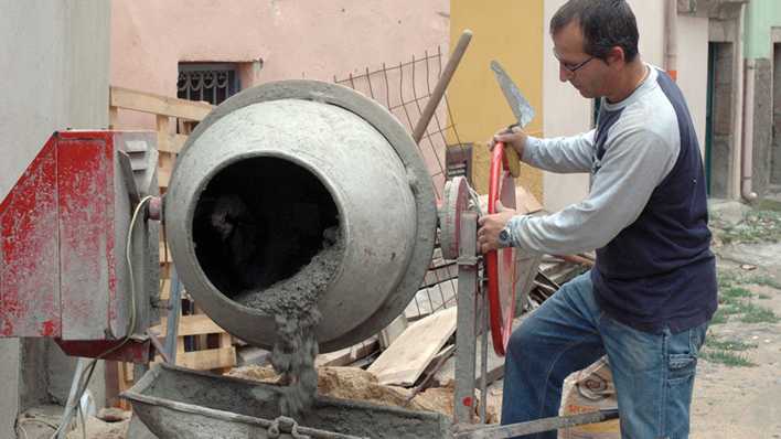 Ein Mann füllt Zement aus einer Zementmischmaschine in eine Schubkarre (Quelle: rbb/OHRENBÄR/Birgit Patzelt)