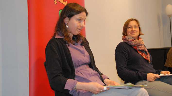 Almut Möhle und Ariane Grundies sitzen mit Manuskripten in den Händen auf der Bühne, im Hintergrund das OHRENBÄR-Banner (Quelle: rbb/OHRENBÄR/Birgit Patzelt)