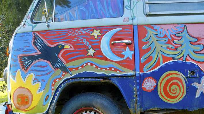 Ein alter, bunt bemalter VW-Bus, mit Vogel, Sternen, Bäumen, Mondsichel usw. (Quelle: imago images/All Canada Photos)