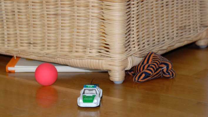 Verschiedene Sachen unter einem Korbsessel: Spielzeug-Polizeiauto, roter Ball, Buch, Puppe (Quelle: rbb/OHRENBÄR/Birgit Patzelt)