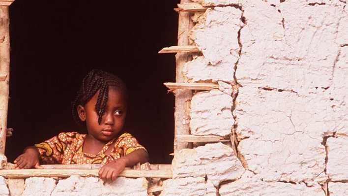 Dunkelhäutiges Mädchen schaut aus einer kleinen afrikanischen Hütte (Quelle: imago images/teutopress)