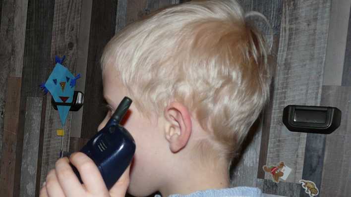 Ein blonder Junge mit einem Handy, im Raum, seitliche Aufnahme (Quelle: rbb/OHRENBÄR/Sonja Kessen)