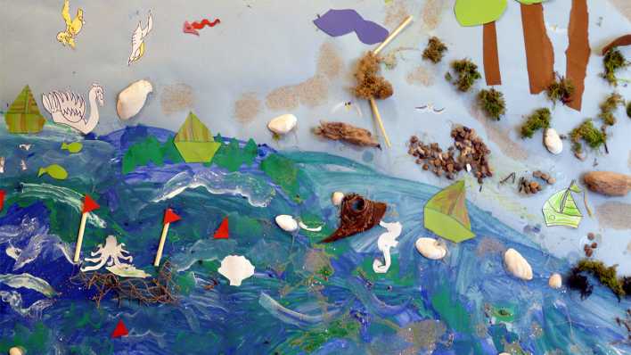 Kinderzeichnung: das blaue Meer mit Meeresbewohnern, Schiffen und einem Strand; Muscheln, Hölzer u.a. Materialien eingearbeitet (Quelle: rbb/OHRENBÄR)