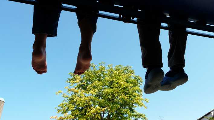 Zwei Beinpaare von Kindern, von unten auf einer Brücke fotografiert, noch zu sehen sind ein Baum und der blaue Himmel (Quelle: rbb/OHRENBÄR/Sonja Kessen)