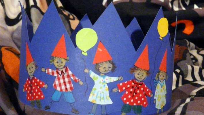 Bastelei: eine blaue Krone, darauf gemalt Kinder mit roten Spitzhüten und Luftballons (Quelle: rbb/OHRENBÄR/Sonja Kessen)