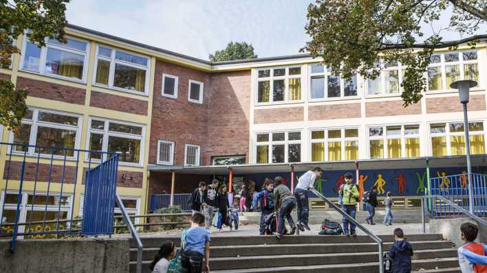 Ein Schulgebäude, davor Kinder und Eltern, an der Wand bunte Keith Haring-Figuren (Quelle: imago images/Lars Berg)